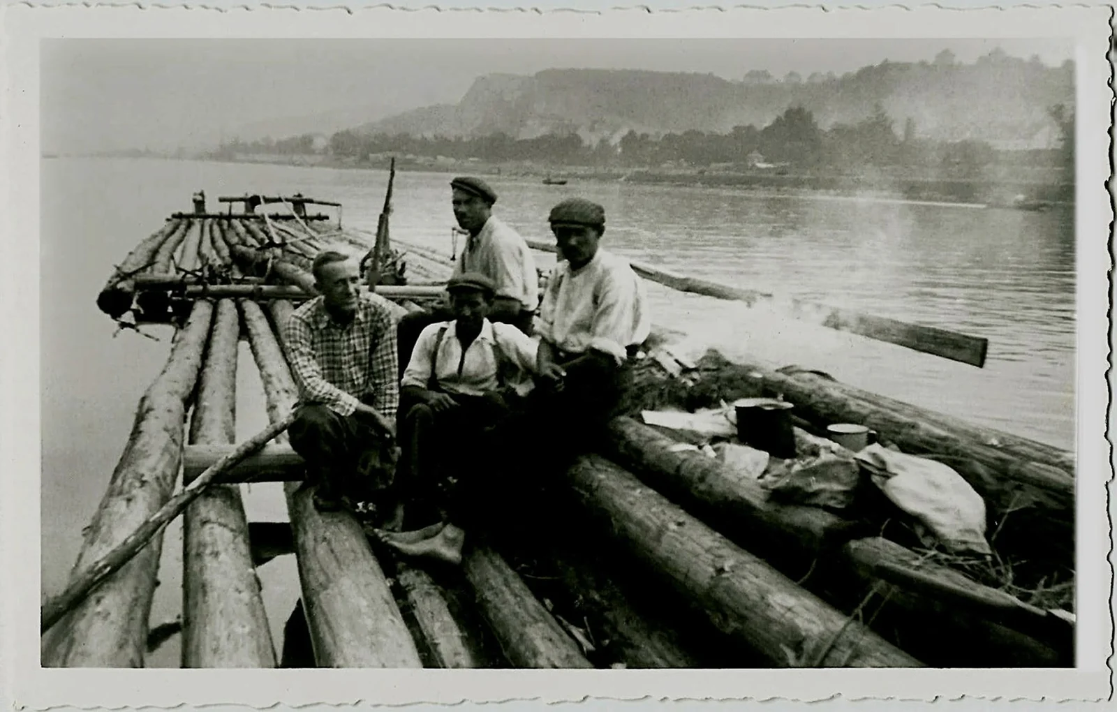 Cuatro almadieros en una balsa de troncos con remos y equipo